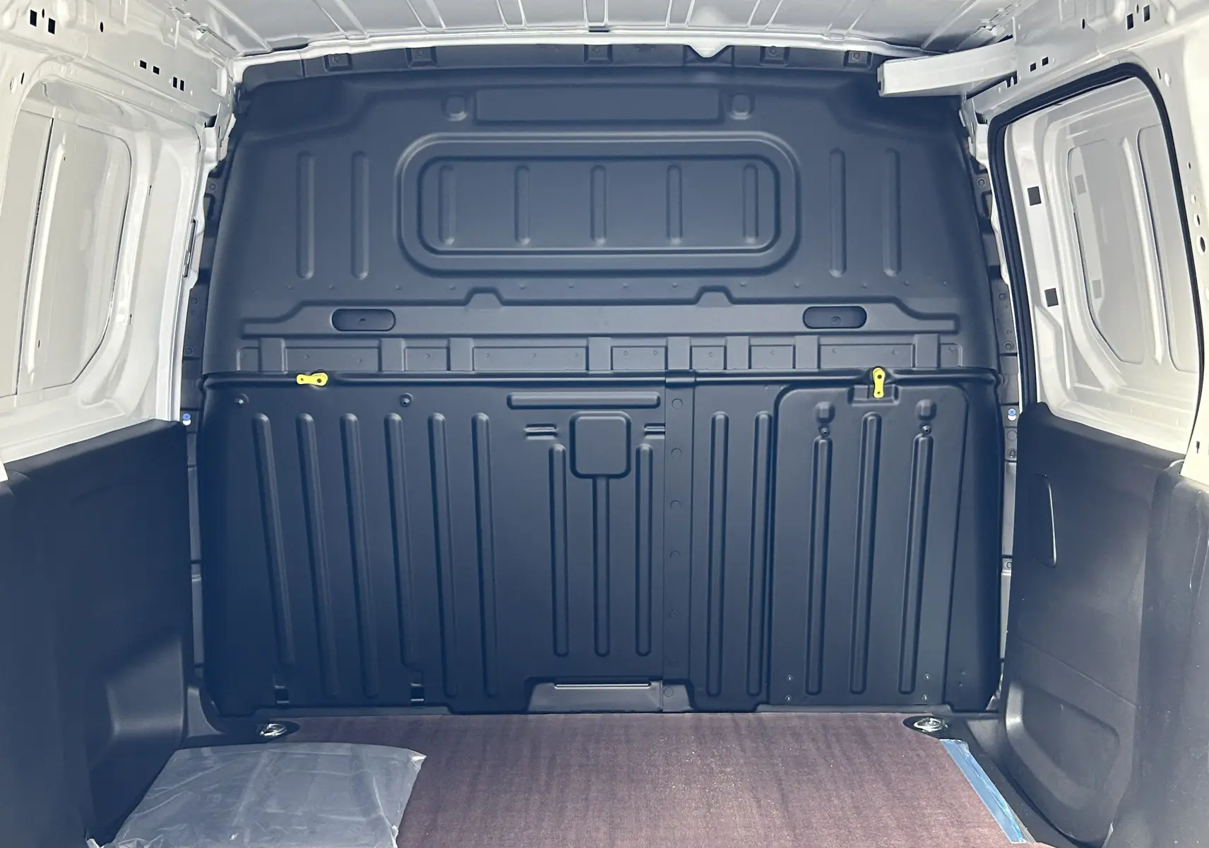 Intérieur du fourgon blanc Peugeot Partner 2025, vue arrière du compartiment de chargement avec plancher bois et paroi noire.