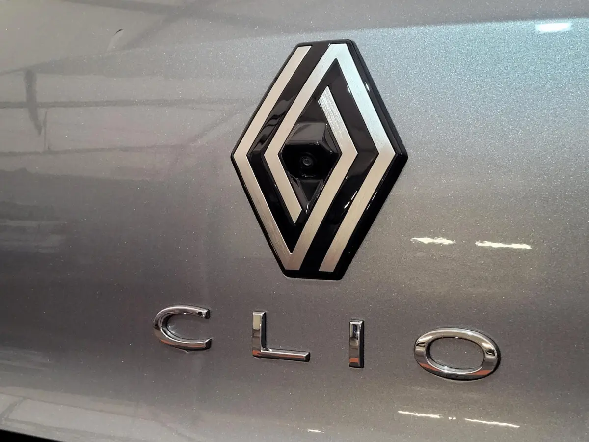 Gros plan sur le logo Renault et le nom Clio en lettres chromées sur la carrosserie gris foncé du coffre arrière.