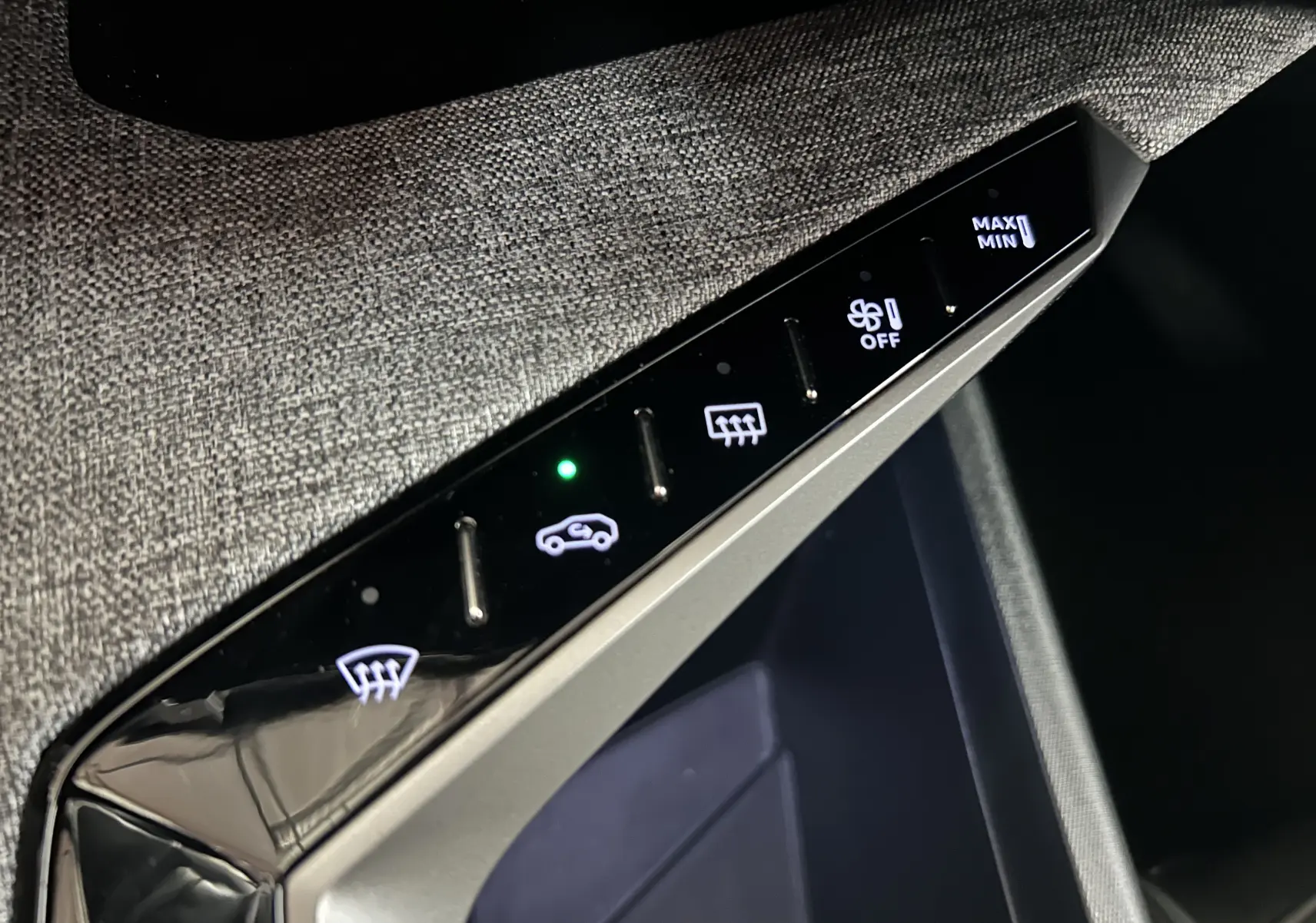 Détail des commandes de climatisation sur la console centrale, avec surface textile grise visible autour.