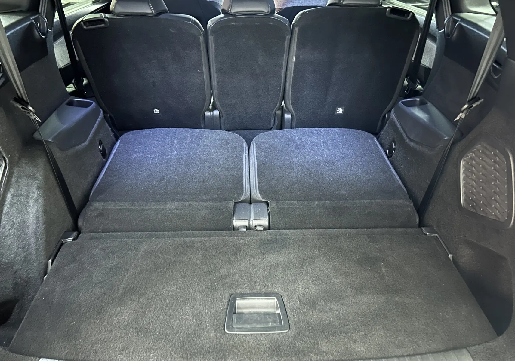 Vue arrière du coffre du Peugeot 5008 hybride 2025, sièges arrière rabattus et revêtement intérieur noir.