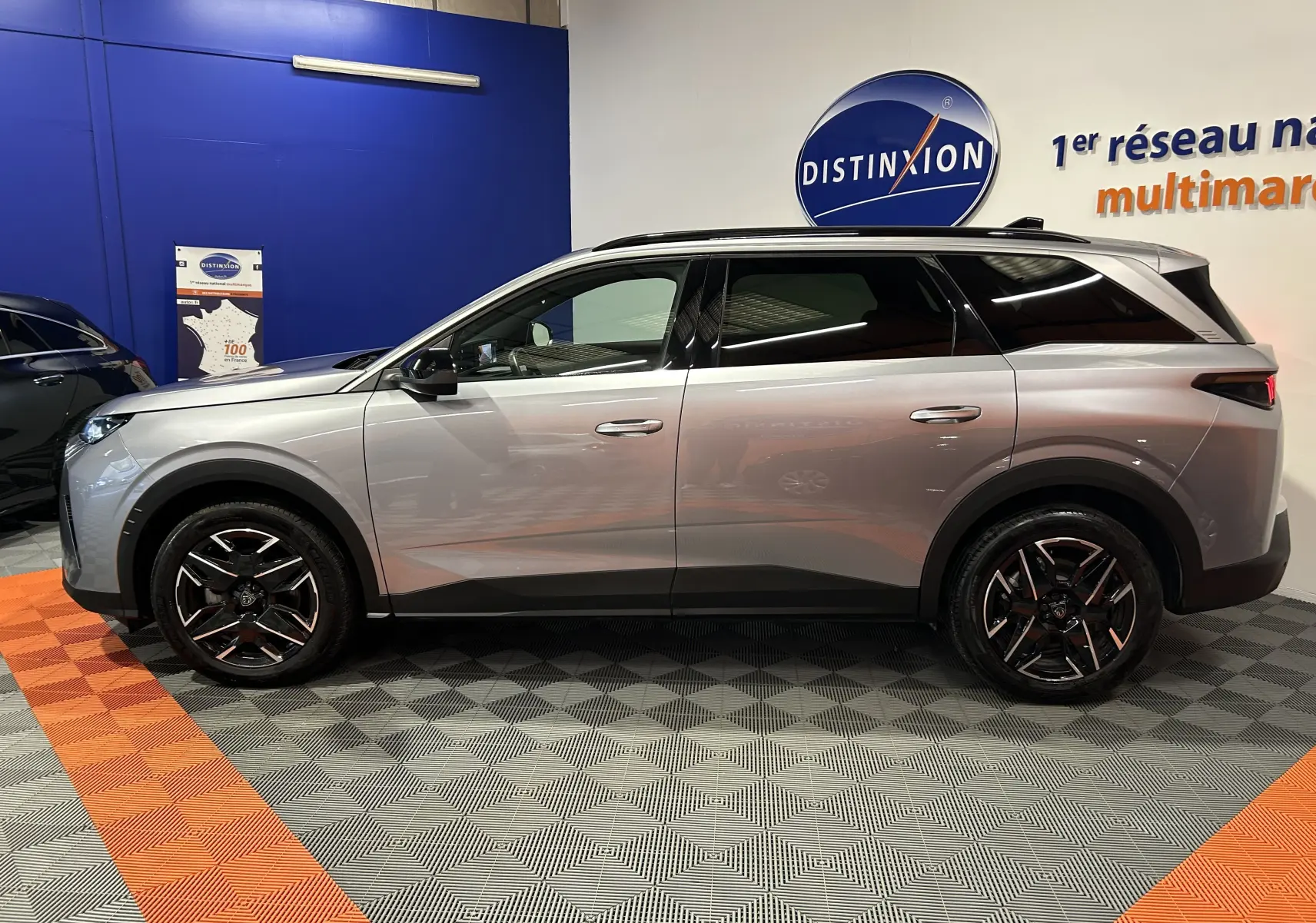 Peugeot 5008 gris Artense vue de profil côté gauche, avec jantes noires et toit panoramique en intérieur showroom.