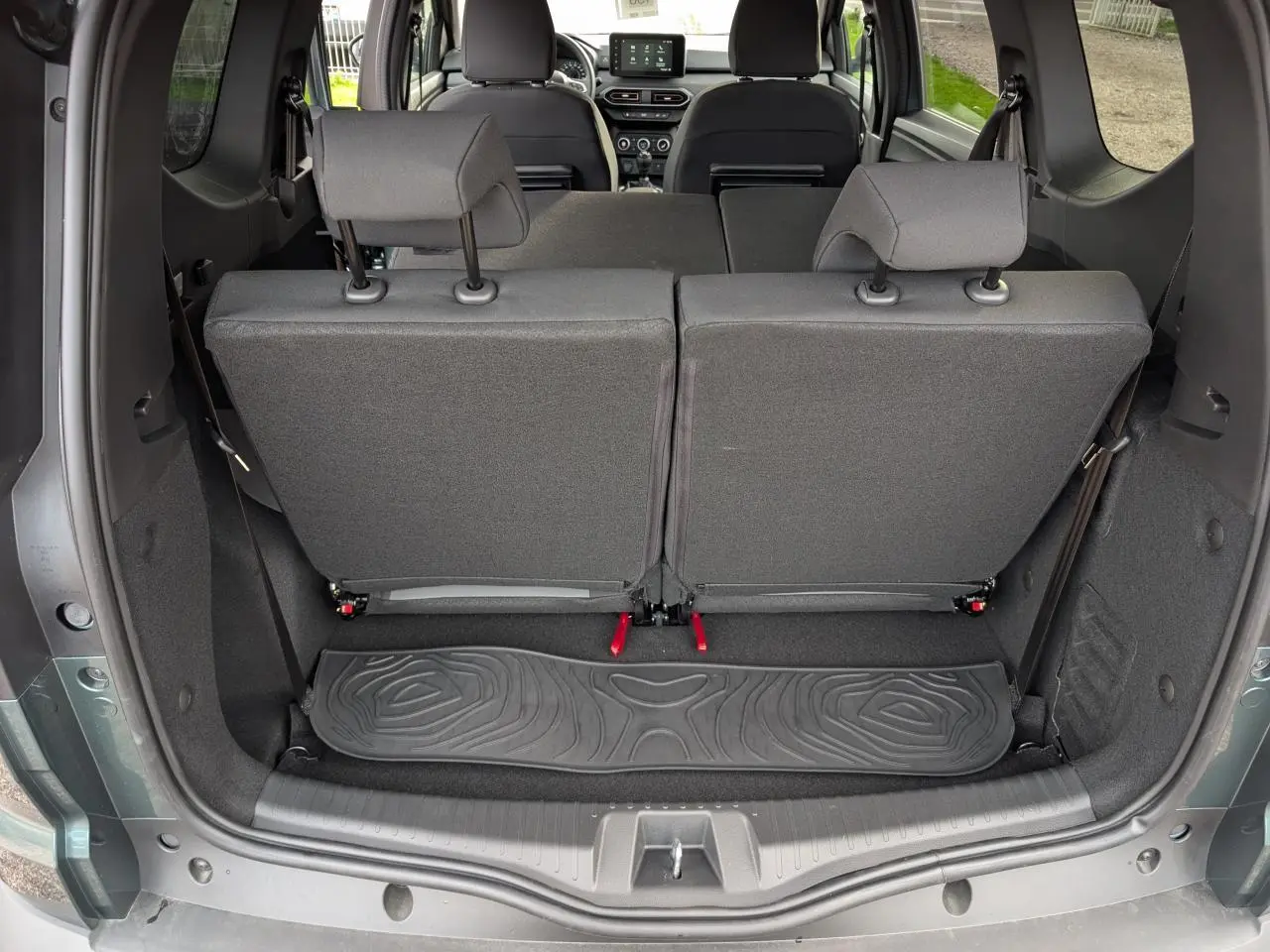 Vue arrière du coffre du Dacia Jogger vert métallisé 2025 avec sièges rabattus et tapis caoutchouc noir.