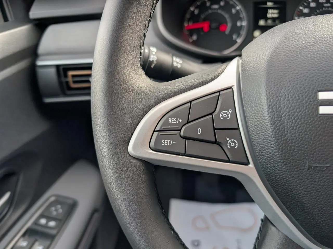 Gros plan sur les commandes de régulateur de vitesse au volant noir du Dacia Jogger 2025, intérieur gris acier.