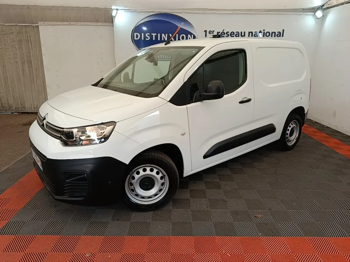 Vue 3/4 avant droit d’un utilitaire Citroën Berlingo blanc avec pare-chocs noirs et jantes acier en intérieur showroom.