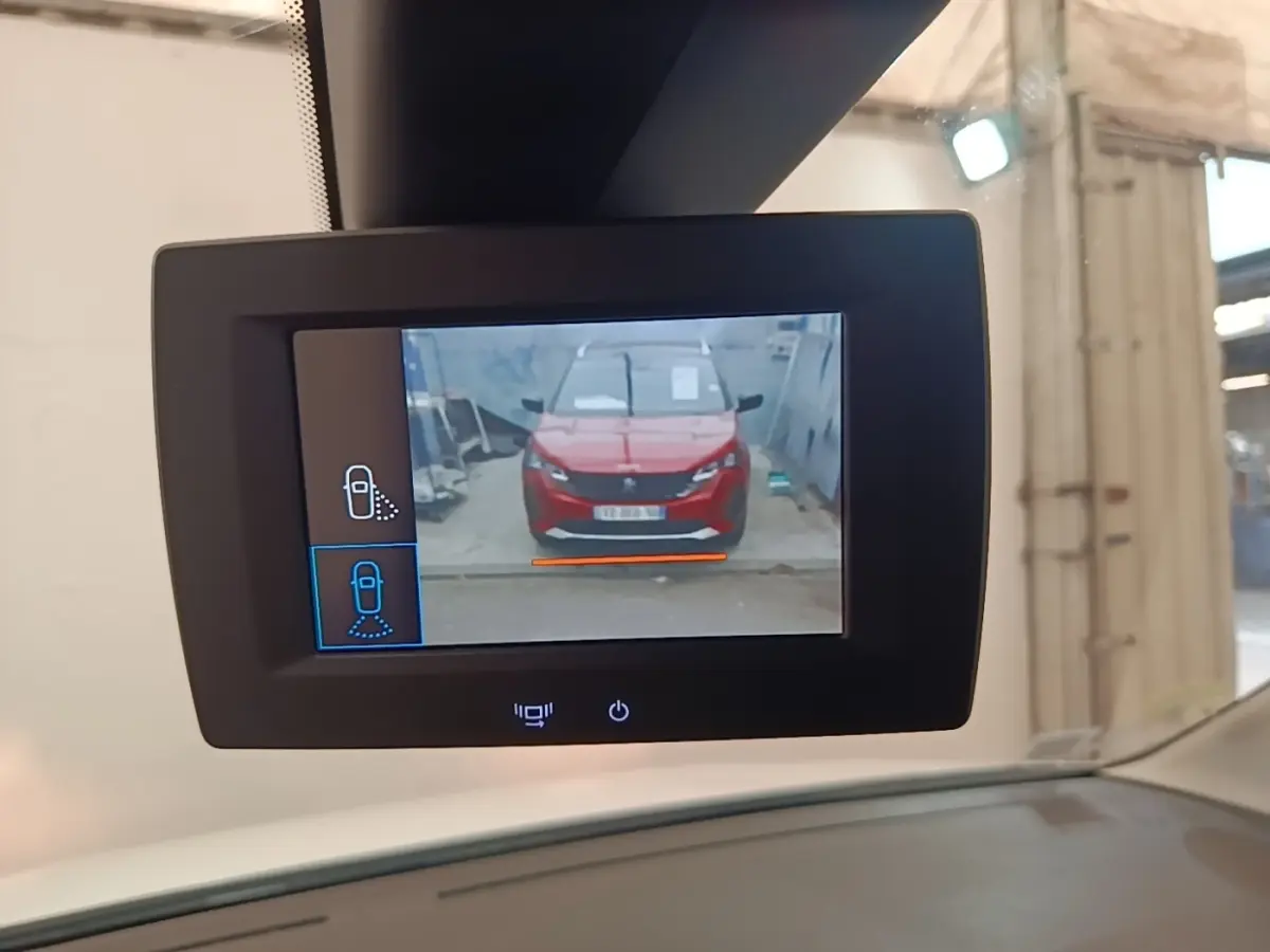 Écran de caméra de recul montrant une voiture rouge vue de face dans un garage, prise depuis l'intérieur.