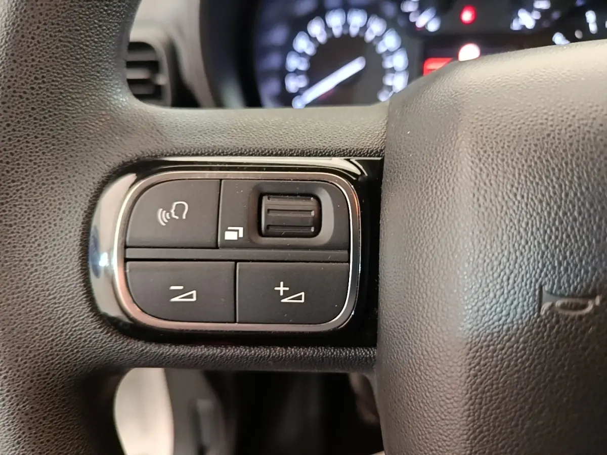 Gros plan sur les commandes du volant noir du Citroën Berlingo 2020, avec tableau de bord flou en arrière-plan.