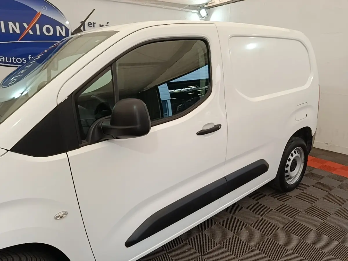 Vue de profil côté gauche d’un utilitaire Citroën Berlingo blanc avec protections latérales noires dans un garage.