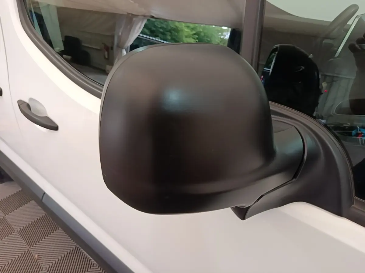 Gros plan sur le rétroviseur noir côté droit d’un Citroën Berlingo blanc, vue latérale avant.