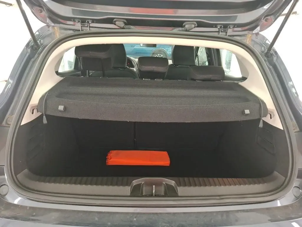 Coffre ouvert vu de l'arrière d'une Renault Clio gris foncé, avec une trousse de secours orange visible à l'intérieur.