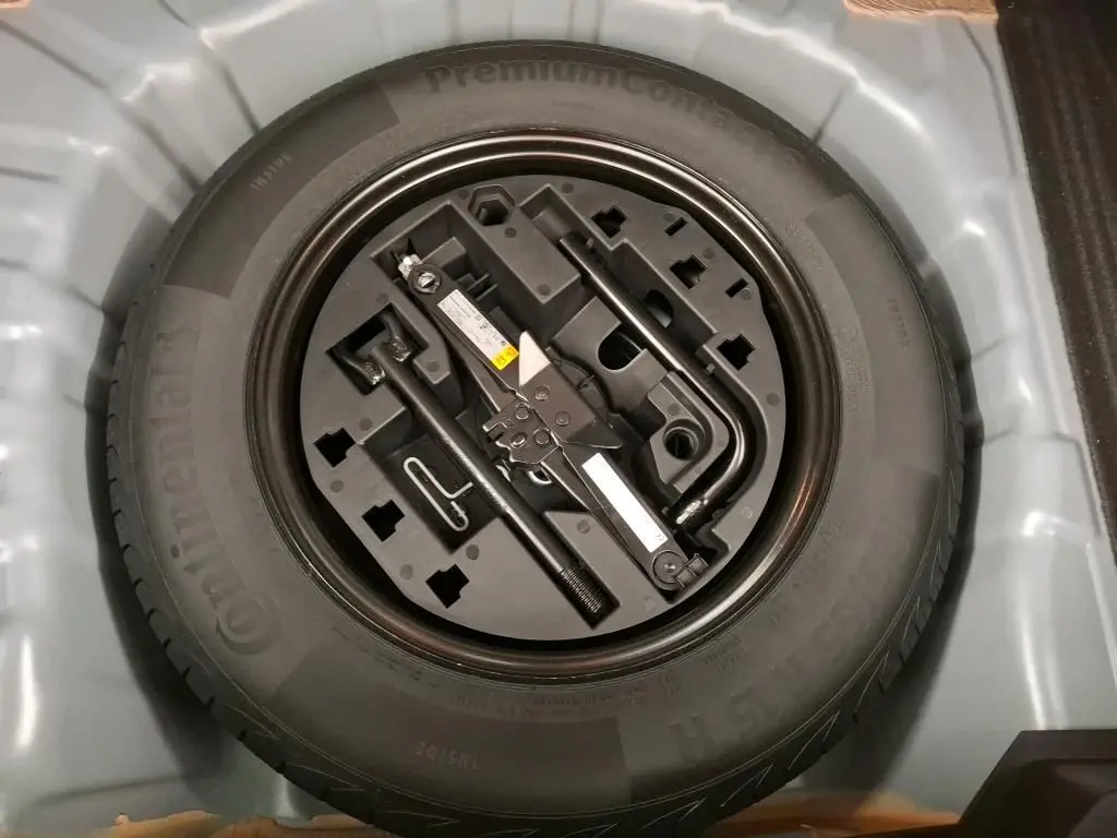 Gros plan sur la roue de secours et le kit d'outils rangés dans le coffre d'une Renault Clio gris foncé.