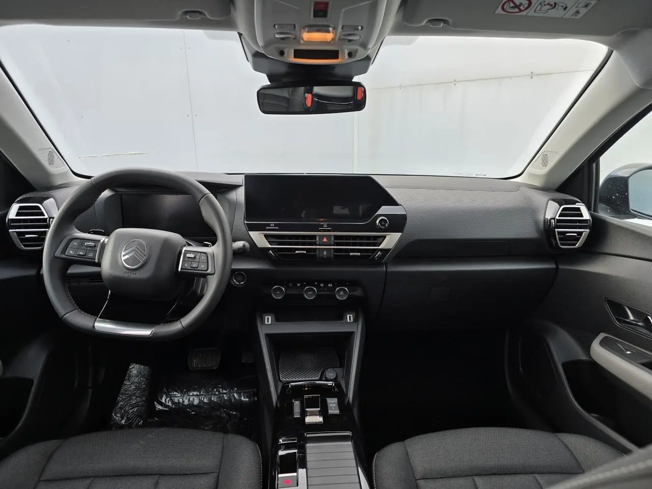 Vue frontale de l'intérieur noir du Citroën C4 III hybride 2025 avec tableau de bord épuré et écran tactile central.