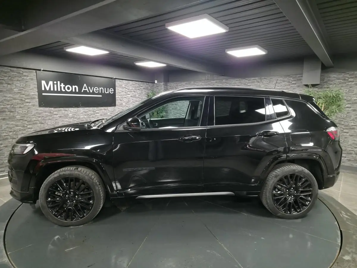 Profil côté gauche d'un Jeep Compass noir brillant avec jantes alliage noires dans un showroom intérieur.