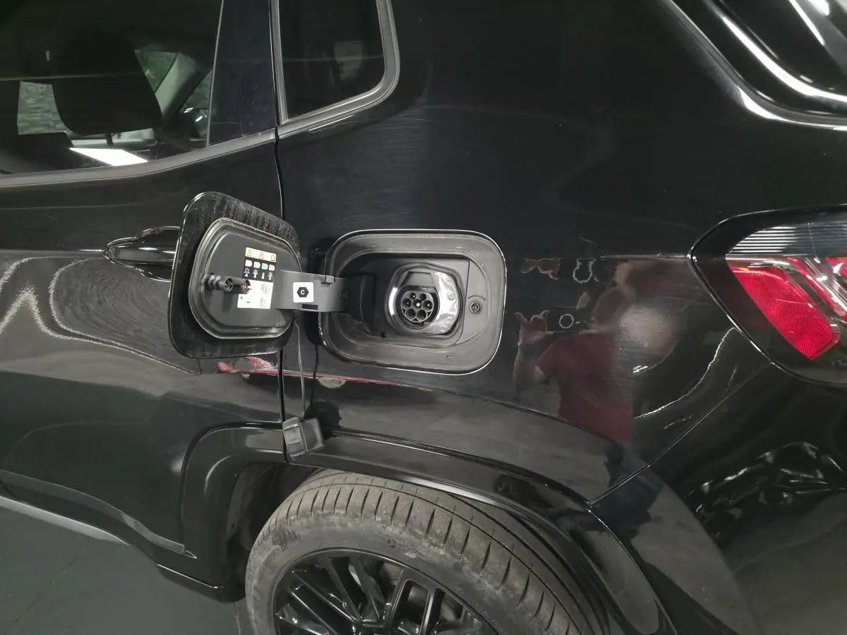 Prise de recharge ouverte côté gauche arrière d'un Jeep Compass noir, mettant en valeur la connectique hybride rechargeable.