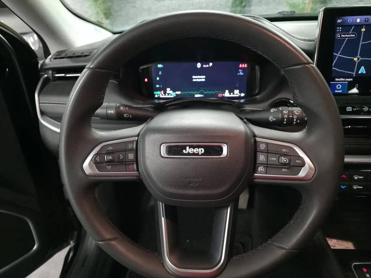 Vue rapprochée du volant cuir noir du Jeep Compass 2022 avec commandes intégrées et tableau de bord numérique.