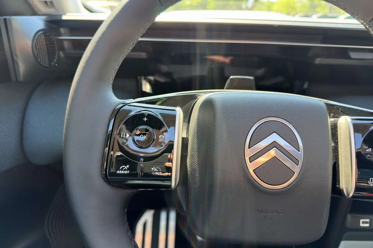 Gros plan sur le volant cuir multifonctions noir avec logo Citroën, tableau de bord numérique en arrière-plan.