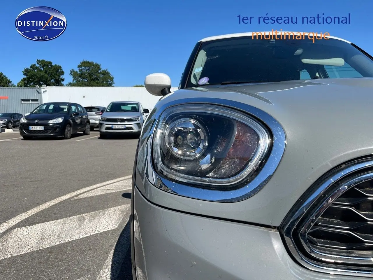 Gros plan sur le phare avant gauche et la calandre chromée d’une MINI Countryman Moonwalk Grey, toit blanc.