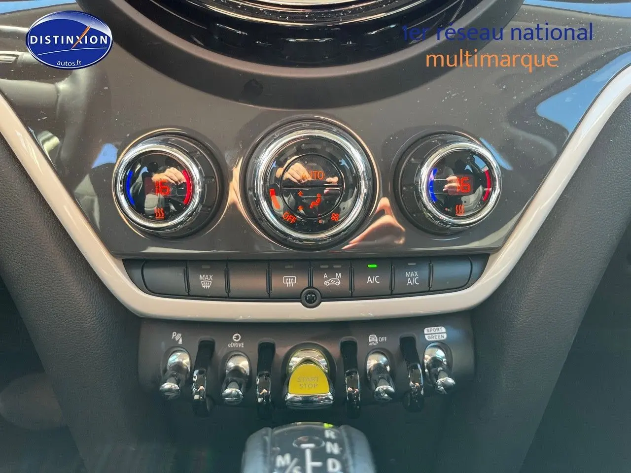 Vue intérieure centrée sur la console centrale du MINI Countryman Cooper SE avec commandes de climatisation et bouton Start/Stop jaune.