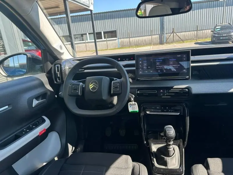 Vue intérieure avant centrée sur le volant Citroën, tableau de bord numérique et levier de vitesse manuel d'une C3 noire 2025.
