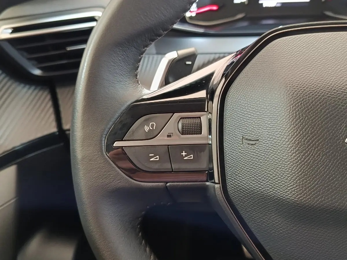 Gros plan sur le volant cuir noir multifonctions côté gauche du Peugeot 2008 blanc, avec commandes audio intégrées.