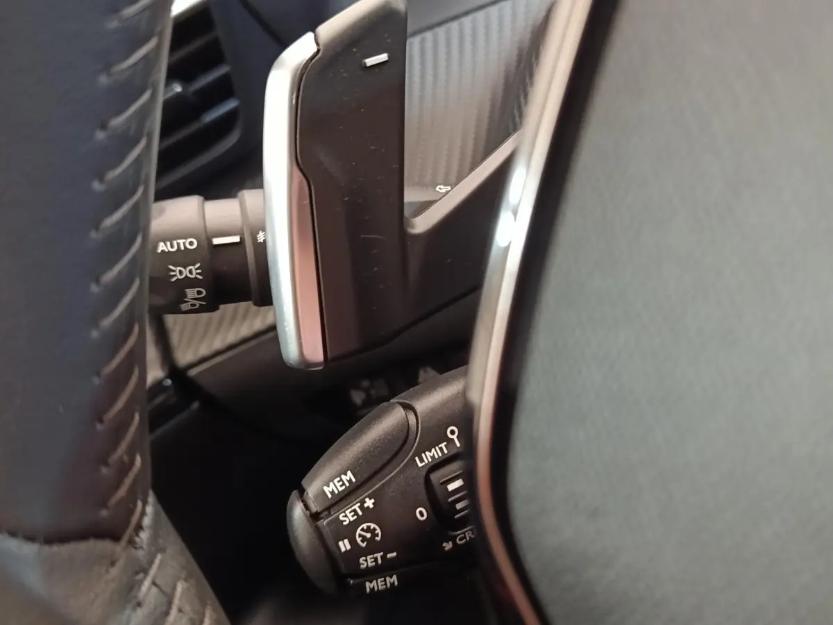 Gros plan sur le volant cuir noir de la Peugeot 2008 2021, montrant les commandes de régulateur de vitesse et éclairage.