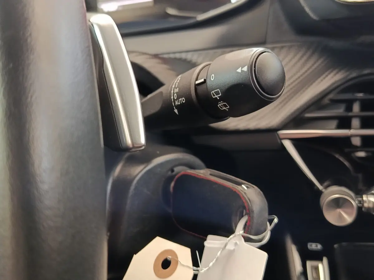 Gros plan sur la commande d’essuie-glace et le volant cuir du Peugeot 2008 blanc, intérieur avec détails carbone.