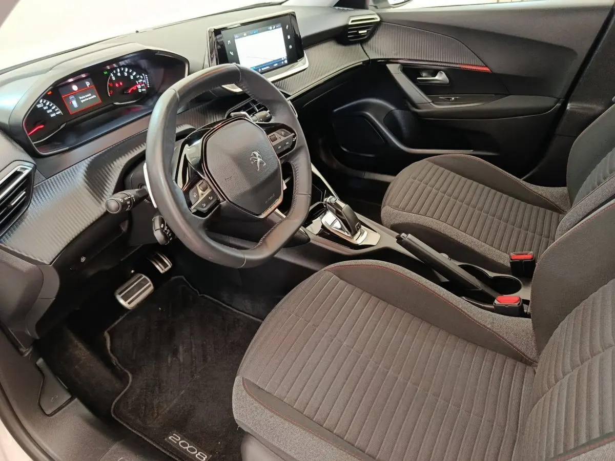 Vue intérieure côté conducteur du Peugeot 2008 2021, volant cuir multifonctions et sièges tissu gris avec surpiqûres rouges.