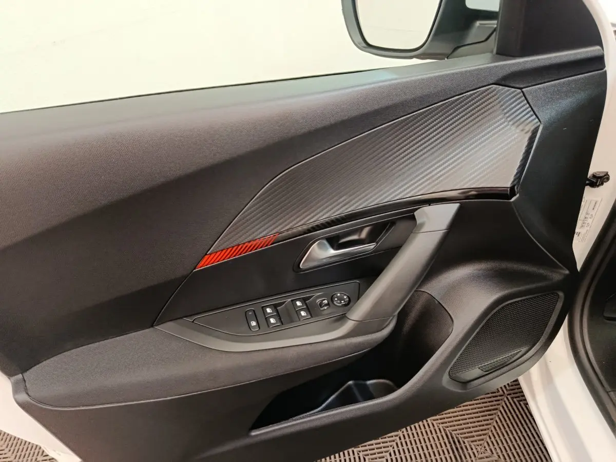 Vue intérieure de la porte avant gauche d’un Peugeot 2008 blanc, avec insert décoratif gris et bande rouge.