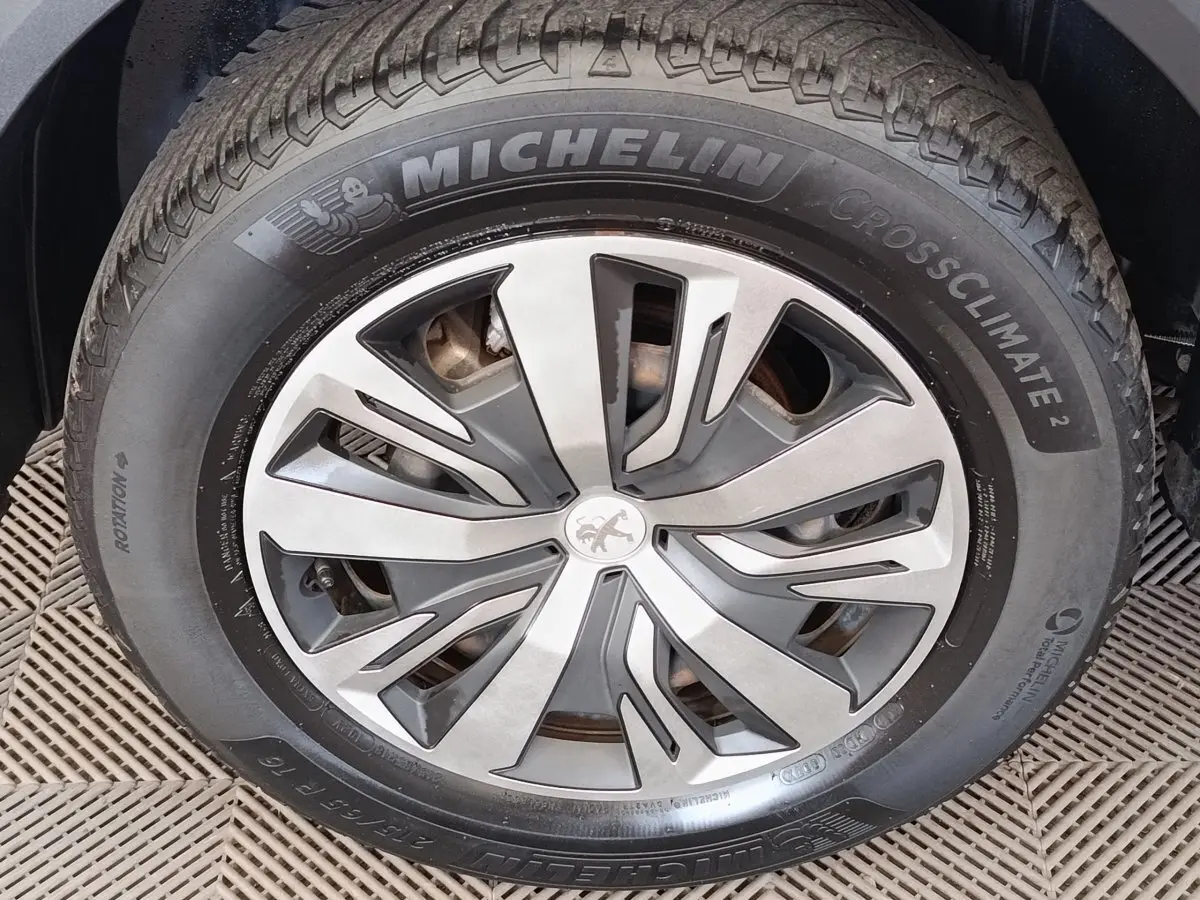Gros plan sur la roue avant droite d’un Peugeot 2008 blanc, avec jante alliage et pneu Michelin CrossClimate.