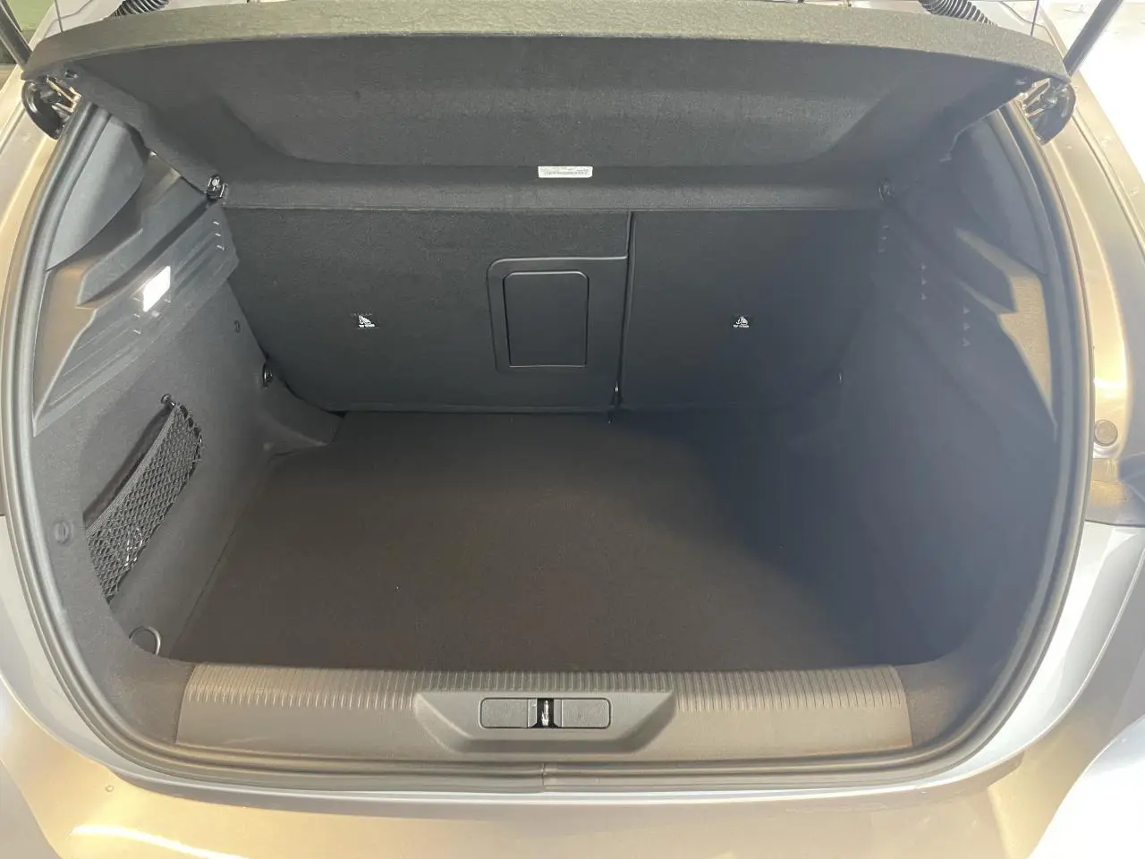Coffre ouvert vu de l'arrière d'une Peugeot 308 gris Artense avec intérieur noir et filet de rangement latéral.