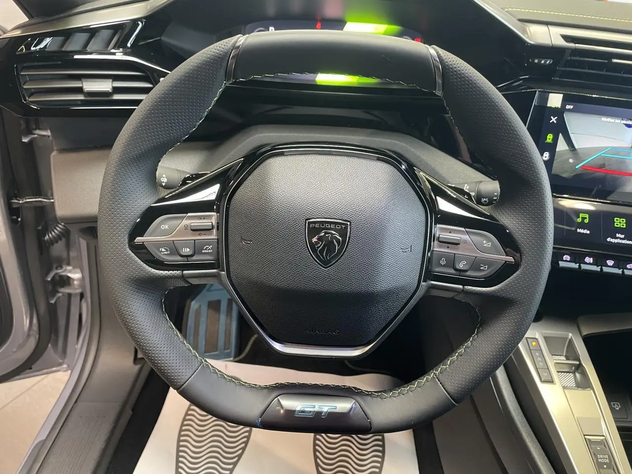 Vue rapprochée du volant GT en cuir noir avec surpiqûres vert Adamite de la Peugeot 308 Gris Artense 2026.