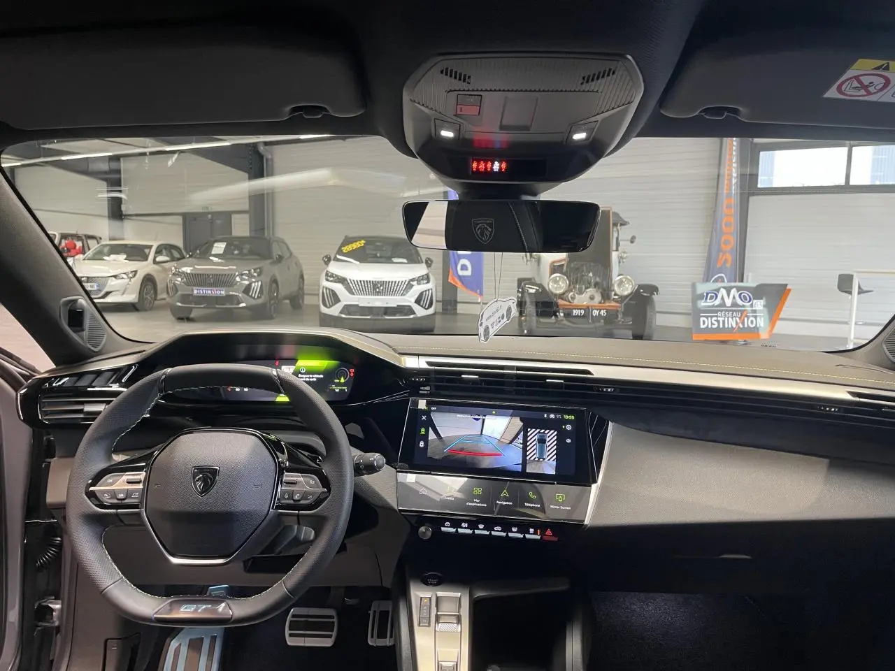 Vue intérieure avant de la Peugeot 308 GT 2026 gris Artense, avec volant compact GT et écran tactile central allumé.