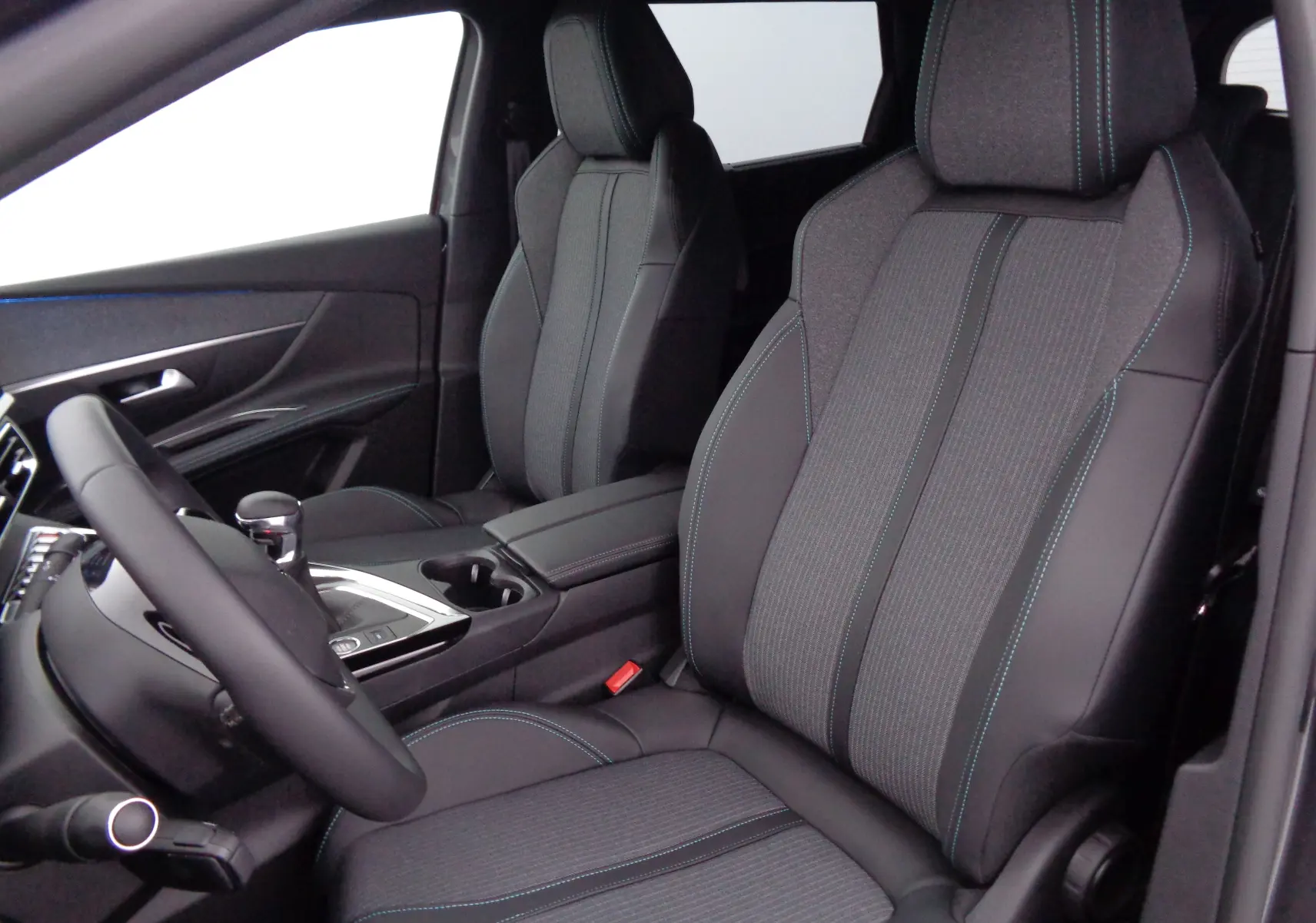 Intérieur avant du Peugeot 5008 2023, sièges gris anthracite avec surpiqûres bleues et console centrale moderne.