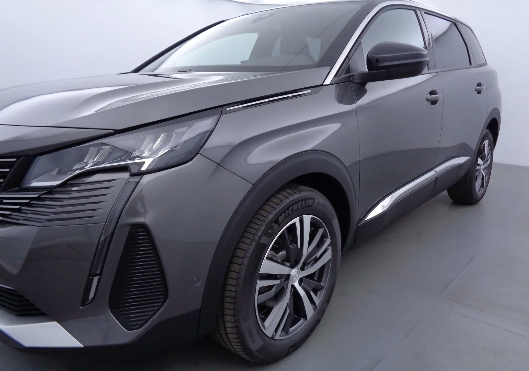 Vue 3/4 avant droit d'un Peugeot 5008 gris platinium métallisé avec jantes alliage et phares LED distinctifs.