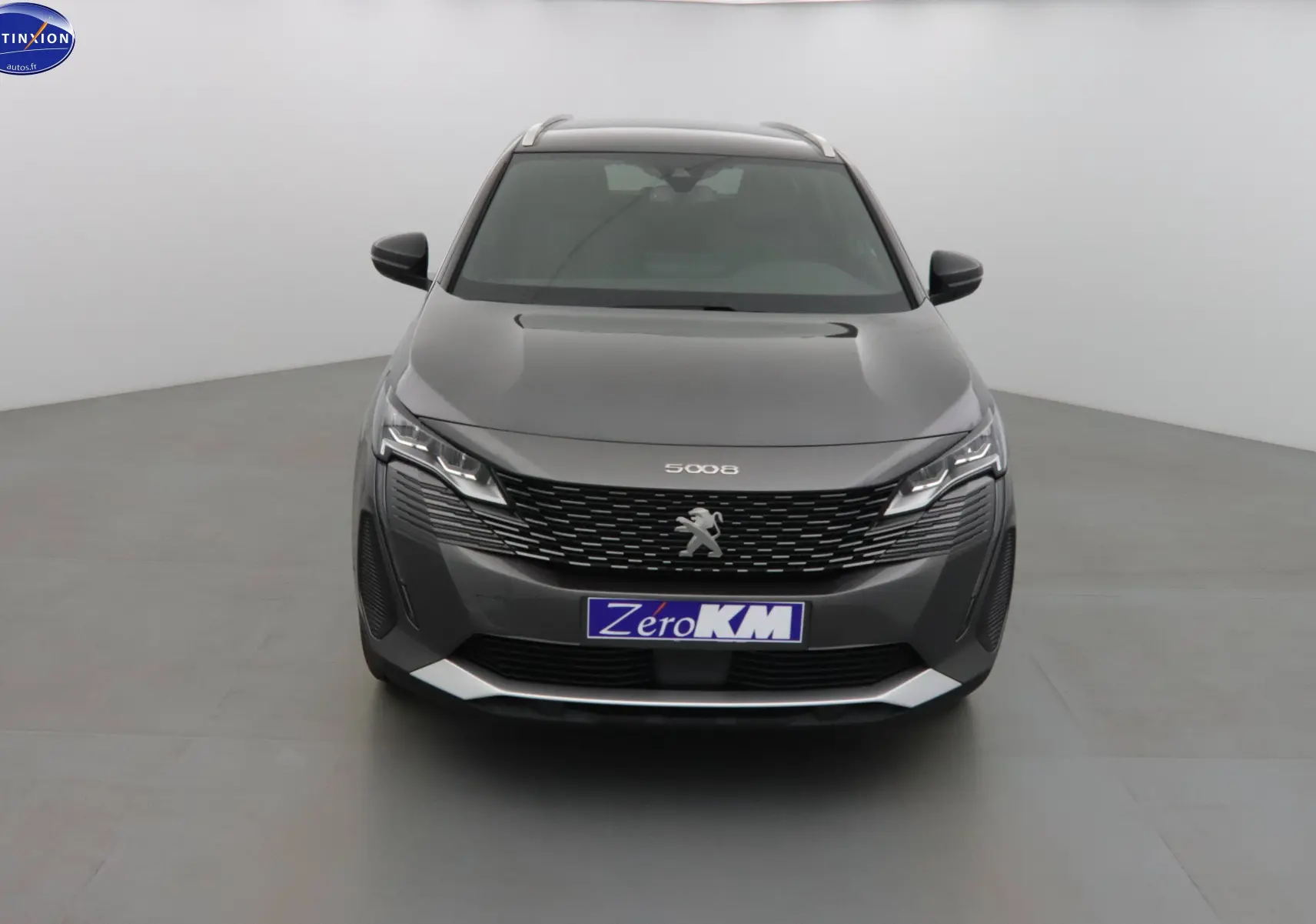 Vue frontale d'un Peugeot 5008 gris platinium métal avec calandre noire et phares LED allumés dans un studio.