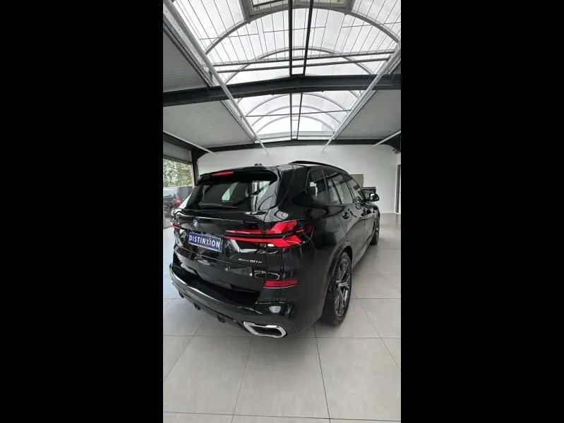 Vue 3/4 arrière droite d'un BMW X5 xDrive50e noir brillant avec feux LED et double sortie d'échappement chromée.