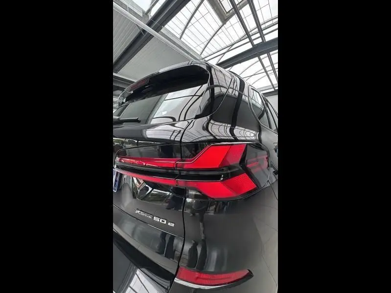 Vue arrière droite d'un BMW X5 xDrive50e noir avec feux LED et badge hybride rechargeable visible dans un showroom lumineux