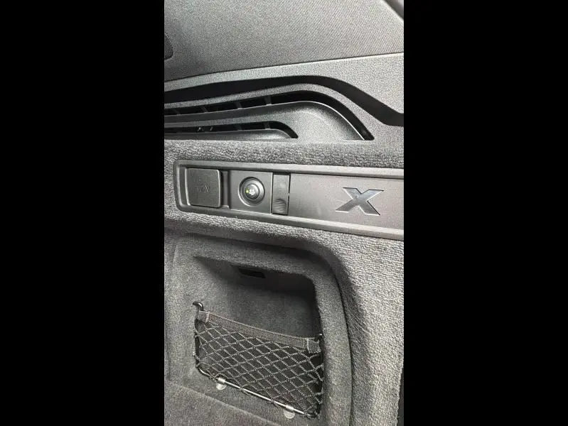 Détail intérieur du coffre noir du BMW X5 xDrive50e 2023 avec filet de rangement et commande électrique.
