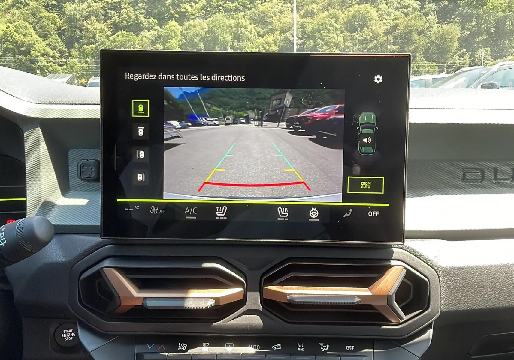 Vue intérieure du tableau de bord du Dacia Duster 2025 blanc, écran tactile affichant la caméra de recul et aérateurs hexagonaux.