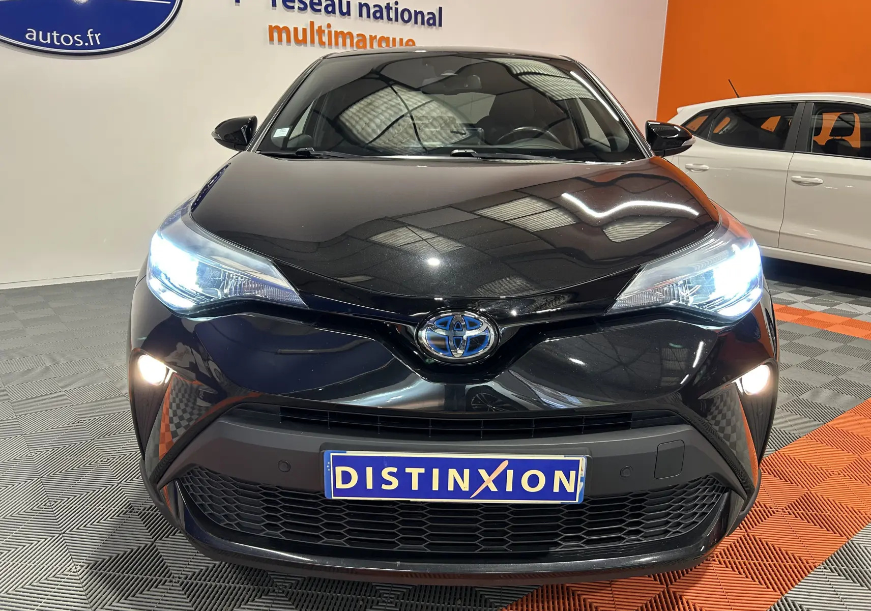 Vue frontale d'un Toyota C-HR Hybride noir métal 2021 avec phares allumés et plaque Distinxion visible.