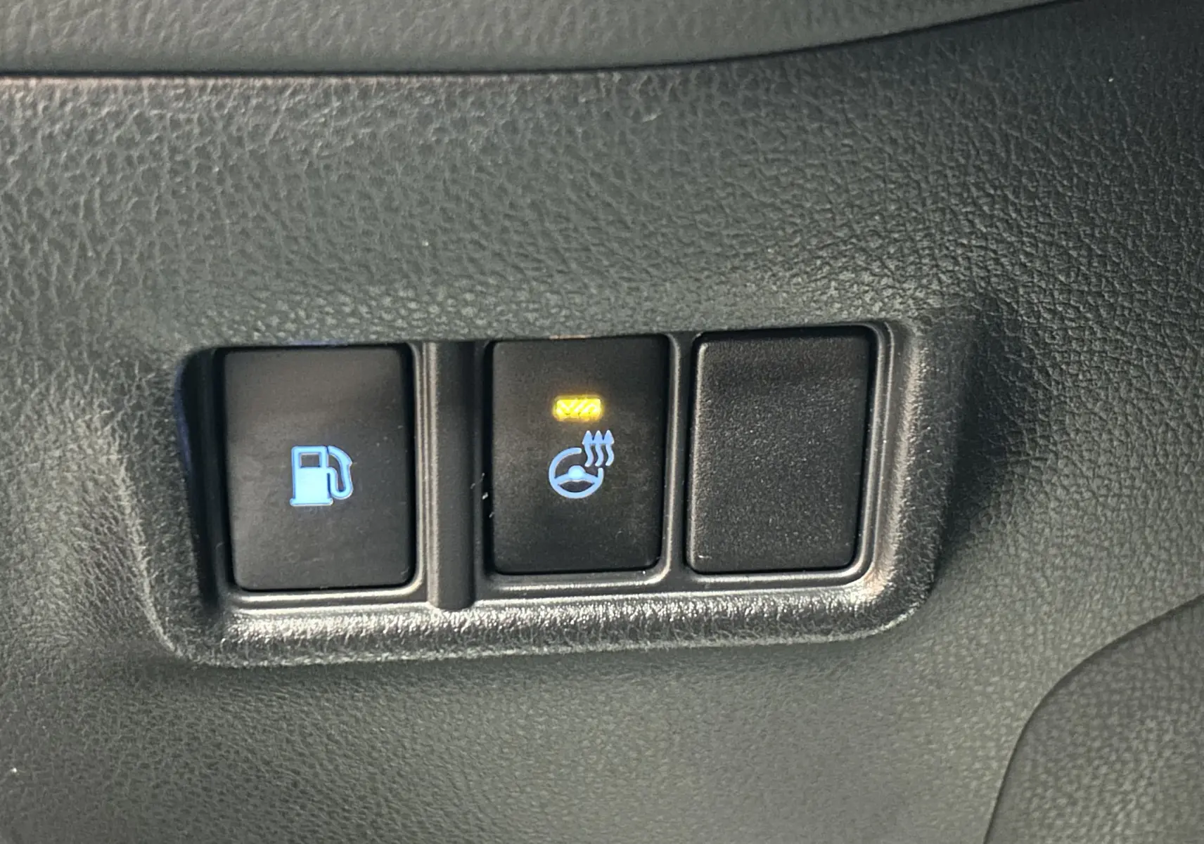 Gros plan sur les boutons de commande intérieurs avec témoin allumé du volant chauffant du Toyota C-HR Hybride noir métal.