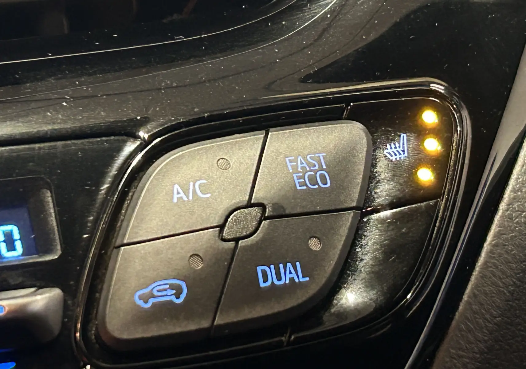 Gros plan sur les commandes de climatisation du Toyota C-HR Hybride noir, avec voyants de siège chauffant allumés.