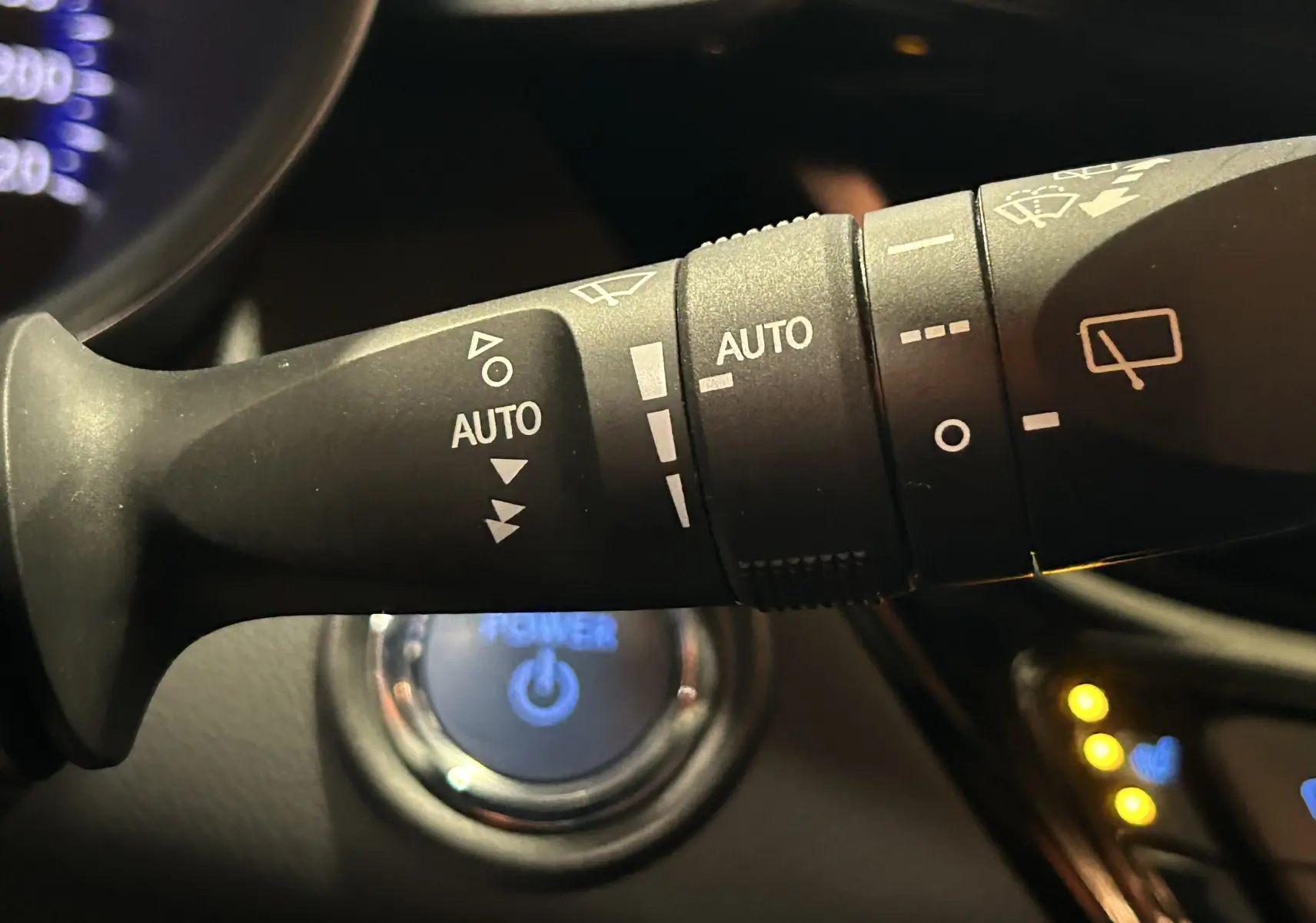 Gros plan sur la commande des essuie-glaces avec fonction auto, volant et bouton start du Toyota C-HR Hybride noir 2021.