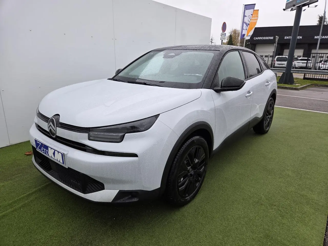 Citroën C4 III hybride blanc Okenite avec toit noir, vue 3/4 avant droit sur parking extérieur humide.