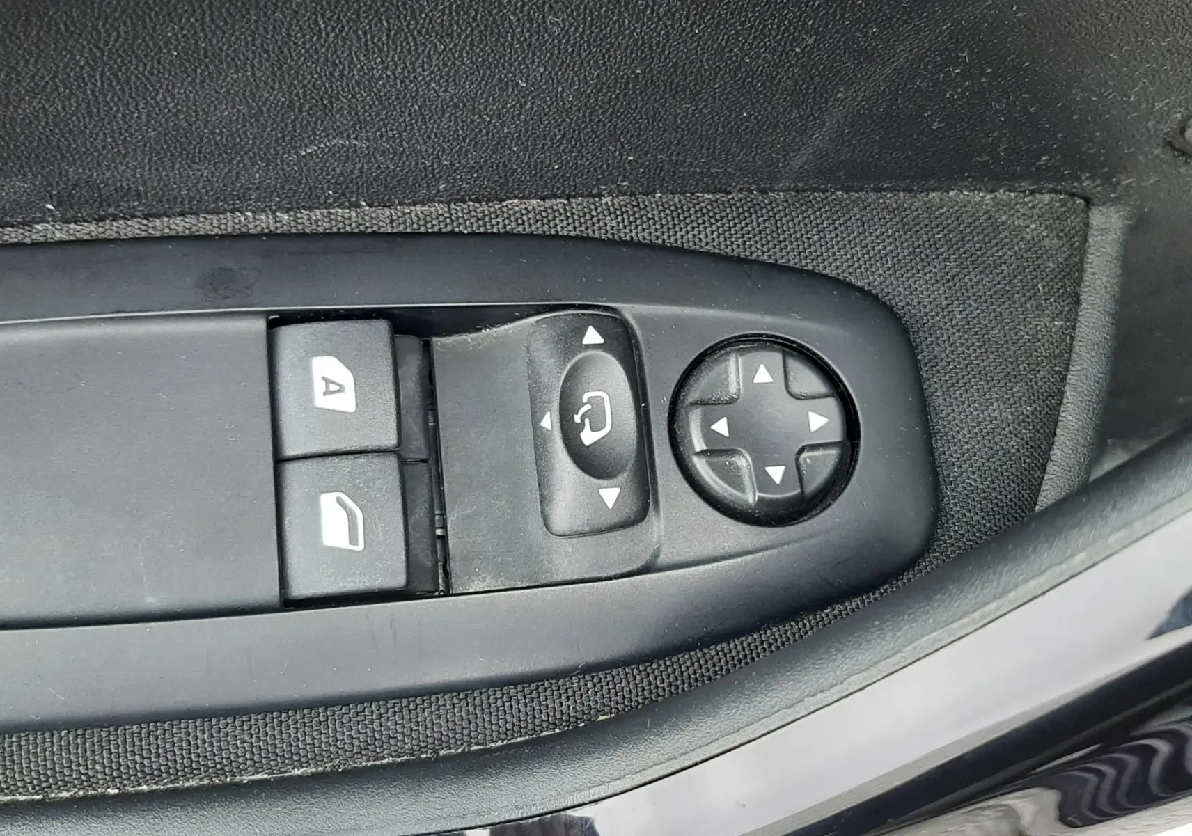 Gros plan sur les commandes de réglage des rétroviseurs et des vitres côté conducteur d'une Peugeot 208 bleu nuit 2019.