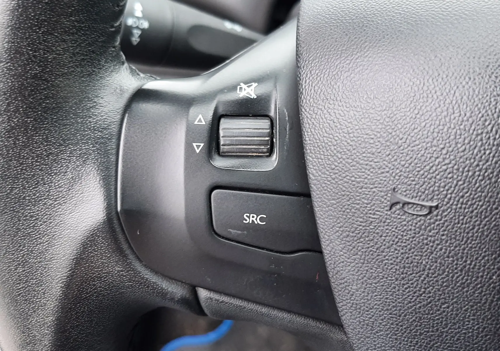 Gros plan sur les commandes du volant noir d'une Peugeot 208 bleu nuit 2019, avec bouton SRC et molette de volume.