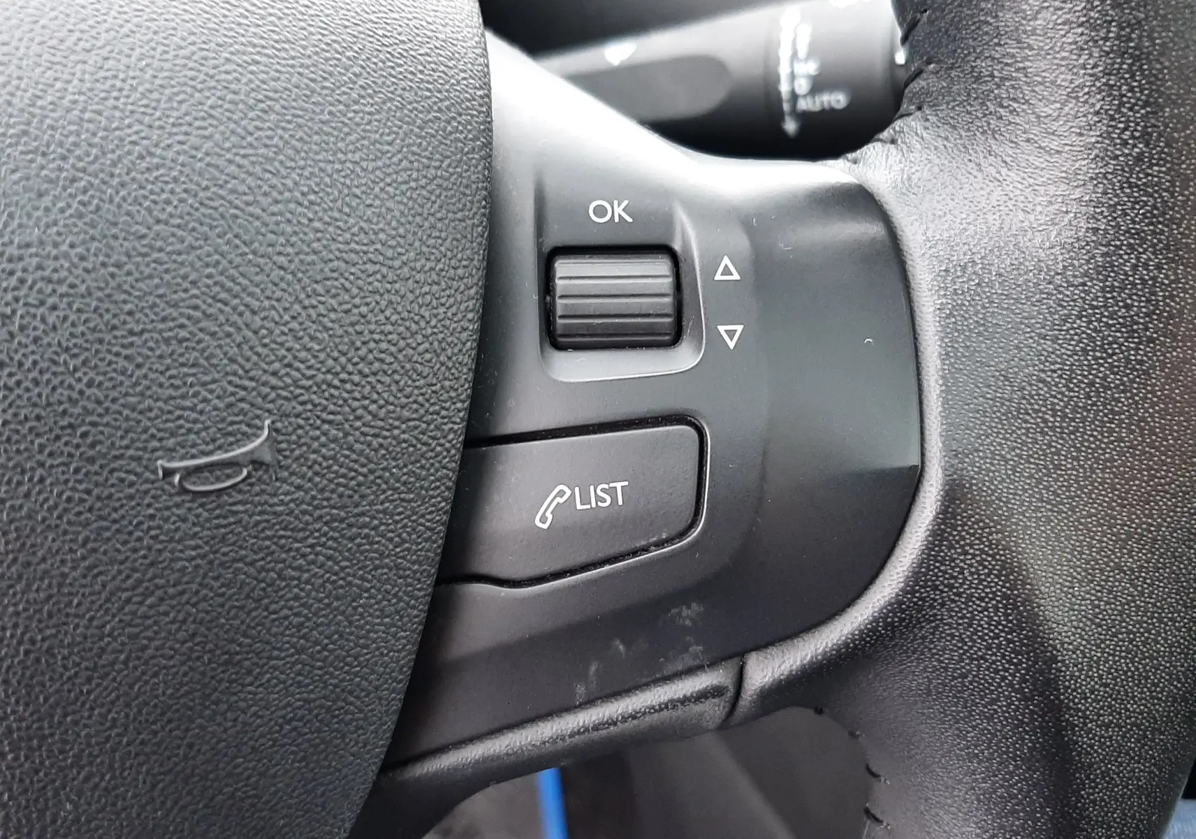 Gros plan sur les commandes gauche du volant noir de la Peugeot 208 bleu nuit, avec bouton OK et fonction liste d'appels.