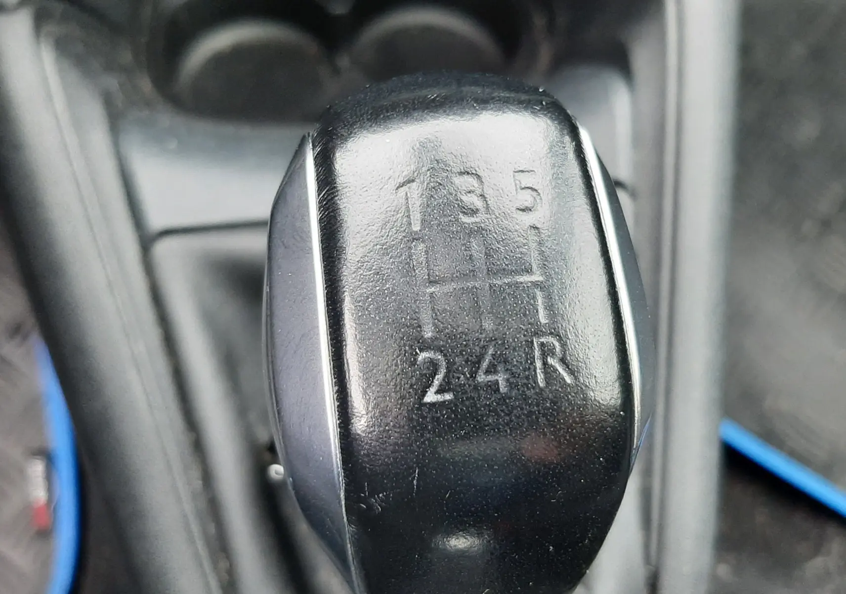 Gros plan sur le levier de vitesse noir manuel de la Peugeot 208 bleu nuit, montrant les positions des 5 rapports et la marche arrière.