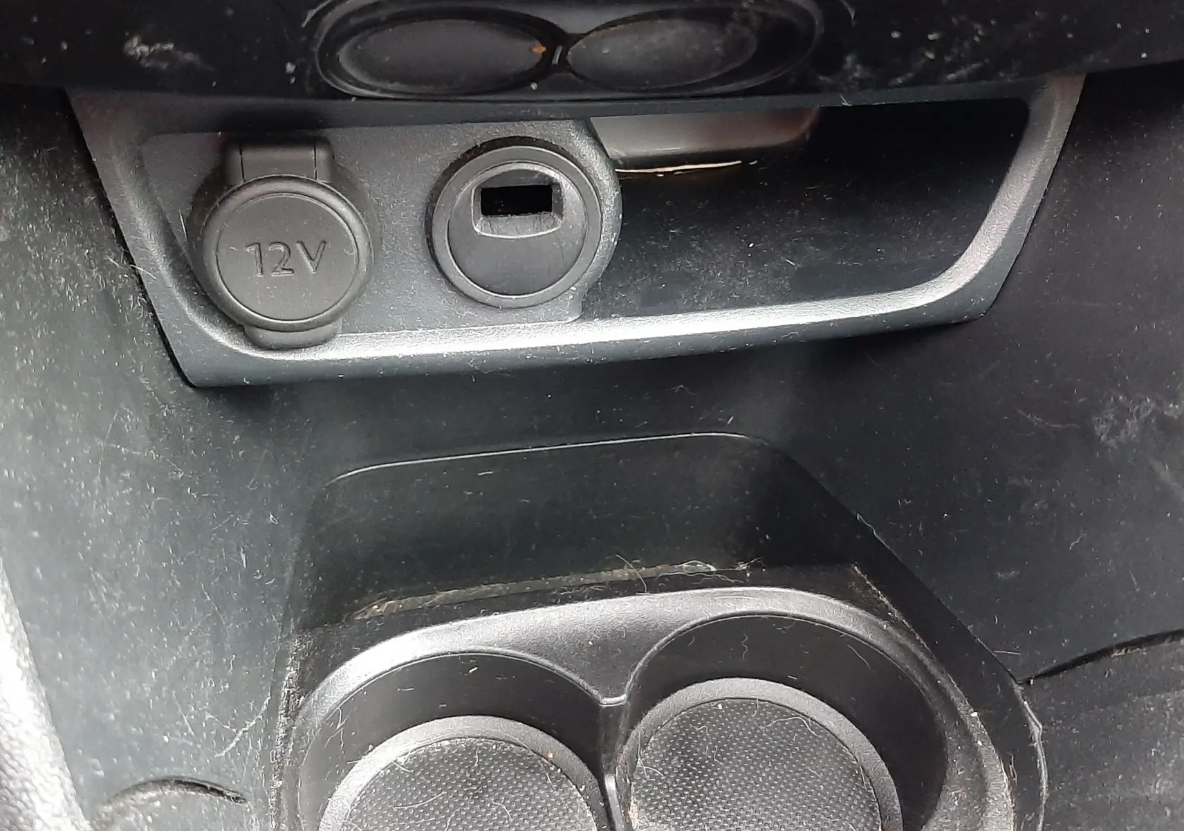 Gros plan sur la console centrale noire du Peugeot 208 bleu nuit, montrant prise 12V et porte-gobelets doubles.