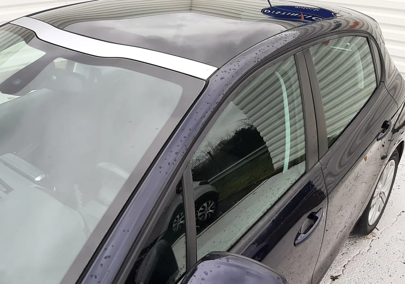 Vue de dessus côté gauche d'une Peugeot 208 bleu nuit 5 portes avec toit panoramique et rétroviseur assorti.