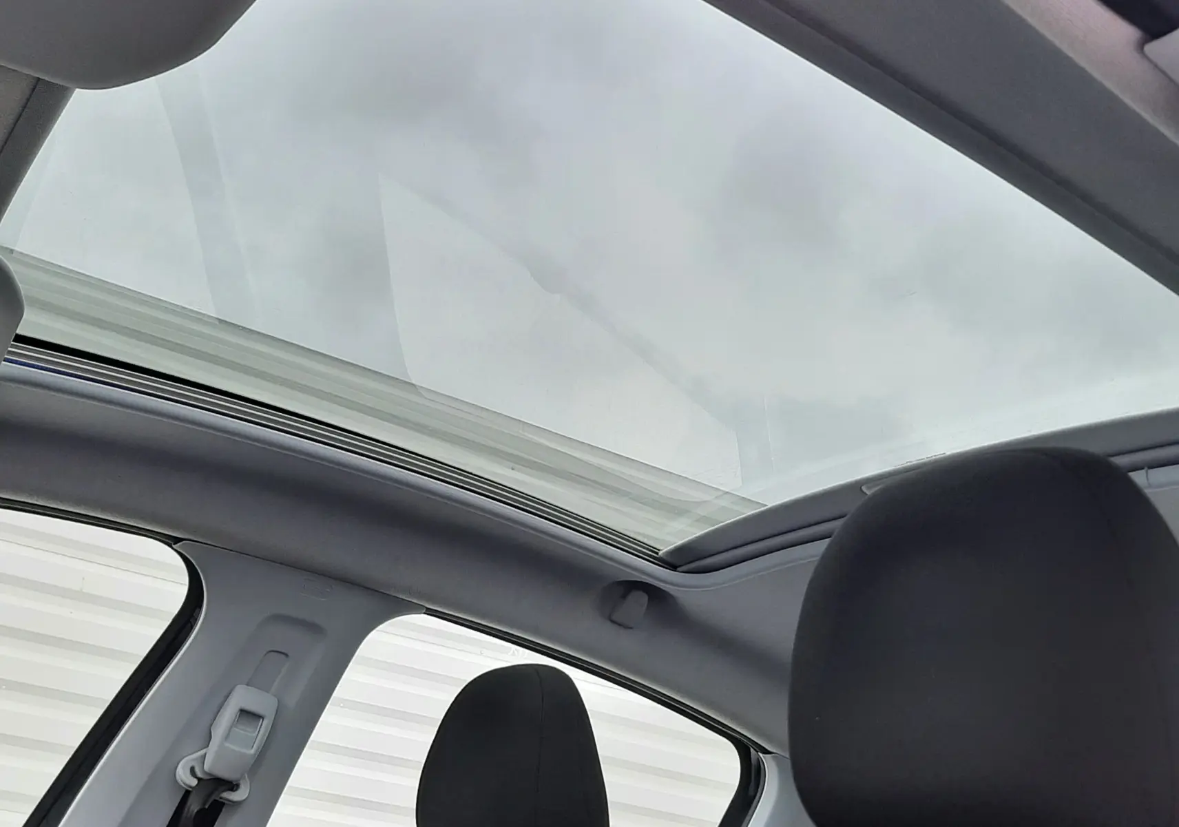 Vue intérieure du toit panoramique et des sièges avant noirs d'une Peugeot 208 bleu nuit 2019.